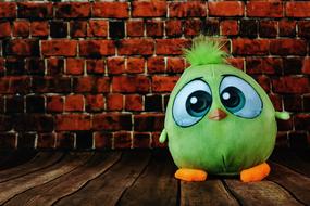 Cute green bird soft toy with orange paws near the brick wall