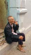 Old man smoking cigar on step at wall, Cuba, havana