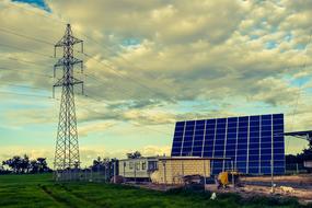 Photo voltaic solar panel, among the green meadow with the tower, under the colorful sky with clouds