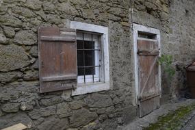 grated window and closed door in old stone building Wall