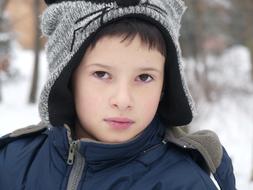 Boy in winter clothes near the trees in snow in winter