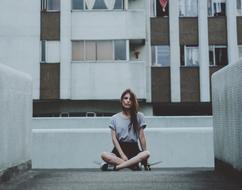 young Woman sits on skateboard at facade of apartments