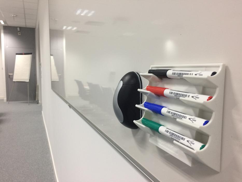 Colorful pens on the stand and eraser, on the shiny whiteboard