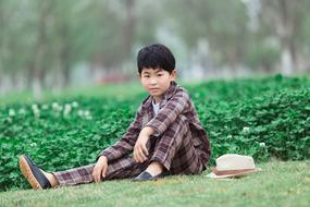 Asian boy sitting on a lawn in a park