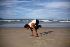 Indian guy, doing yoga on the sandy beach, near the water with the waves