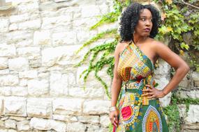 Woman posing in colorful dress with patterns, near the stone wall with plants