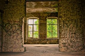 Old, brick house, with the colorful graffities, and view on the green plants, in light, through the windows