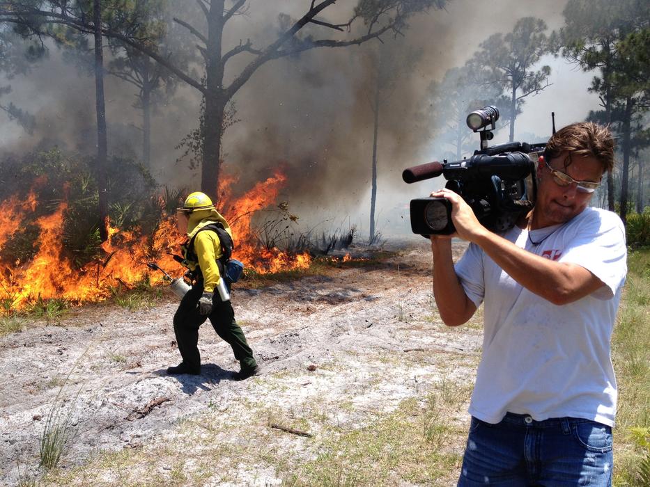 a burning fire in the woods and a man with a camera.