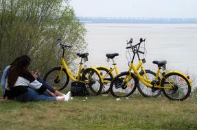 couple is sitting on the riverbank near parked bicycles