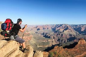 young Man with Backpack sits on rock at scenic landscape