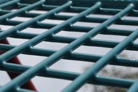 Close-up of the green, metal grid, at blurred background with the trees