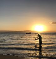 Fisherman with net standing in water on beach at sunset