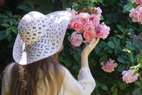 girl in a white hat near a bush with roses