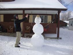 young boy holding hands with Snowman in front of house