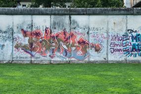 Old wall with colorful graffities near the green grass in Berlin, Germany