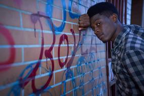 black guy leaned on graffiti wall