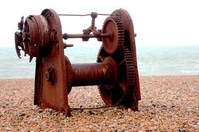 rusty industrial machine stands on a pebble beach