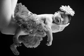 Black and white photo of the newborn baby in dress and with flower on the hands