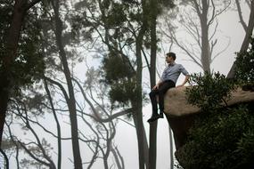young man sits on the edge of a cliff on a background of fog