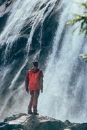 man stands on rock in front of waterfall