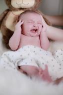 Baby boy crying with hands at head
