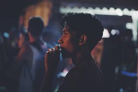 dark photo of a young man is smoking a cigarette