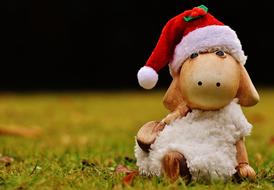 Cute, colorful and beautiful figure of the Christmas sheep in the red and white Santa hat, on the colorful grass