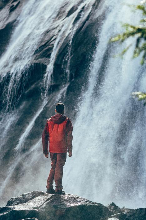 man stands on rock in front of waterfall