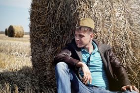 young man in a military cap near a haystack