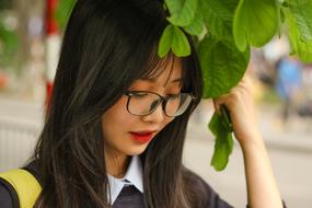young asian Girl in glasses beneath tree close-up on blurred background
