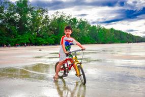 boy riding a bike on the wet sand of the surf
