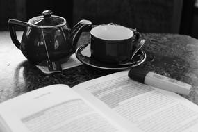 black and white photo of a cup of tea near an open book