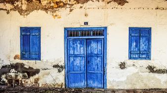 closed blue doors and window shutters on Damaged Wall of Old House