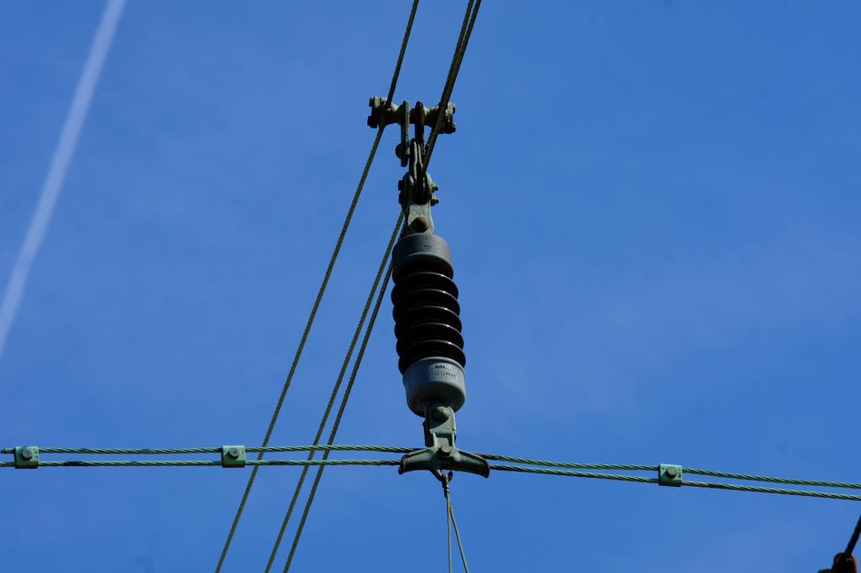 Close-up of the insulator on the cables of the railway, under the blue sky with clouds