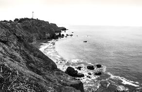 Black and white photo of the beautiful rocky coast of the sea with waves