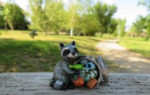 Figure of the cute, beautiful and colorful racoon with the garbage, among the colorful plants