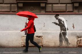 girl with red umbrella walking along wall with graffiti