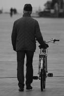 black and white photo of an elderly man walking with a bicycle