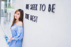 Smiling Asian girl, posing near the "We Seek To Be The Best" sign