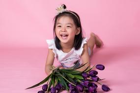 Laughing girl with violet flowers at pink background