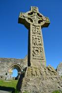 Beautiful high stone cross on the green grass at blue sky background in Ireland