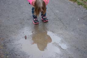 girl looks at reflection in a puddle