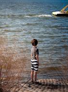 child Boy looking at Boat on Water from beach
