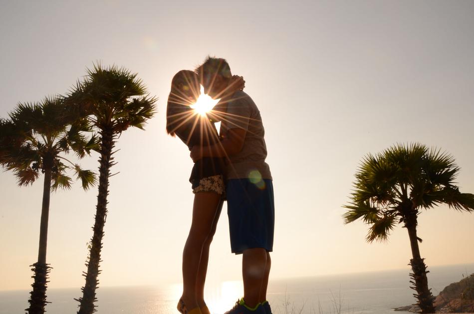 People hugging near the palms at colorful sunset background