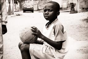 african Child boy sits with ball on street