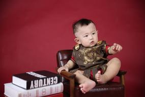 asian baby Boy Sitting on Chair at stack of books