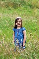 Child girl in blue dress standing in Grass