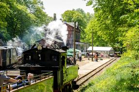 Beautiful, old steam locomotive, on the railway, near the buildings, among the colorful and beautiful plants