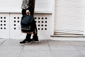 person in Nike sneakers holding backpack in hand