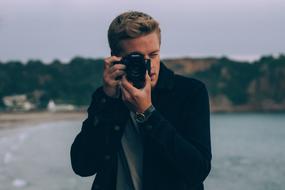 Guy photographer near the water with trees on the shore